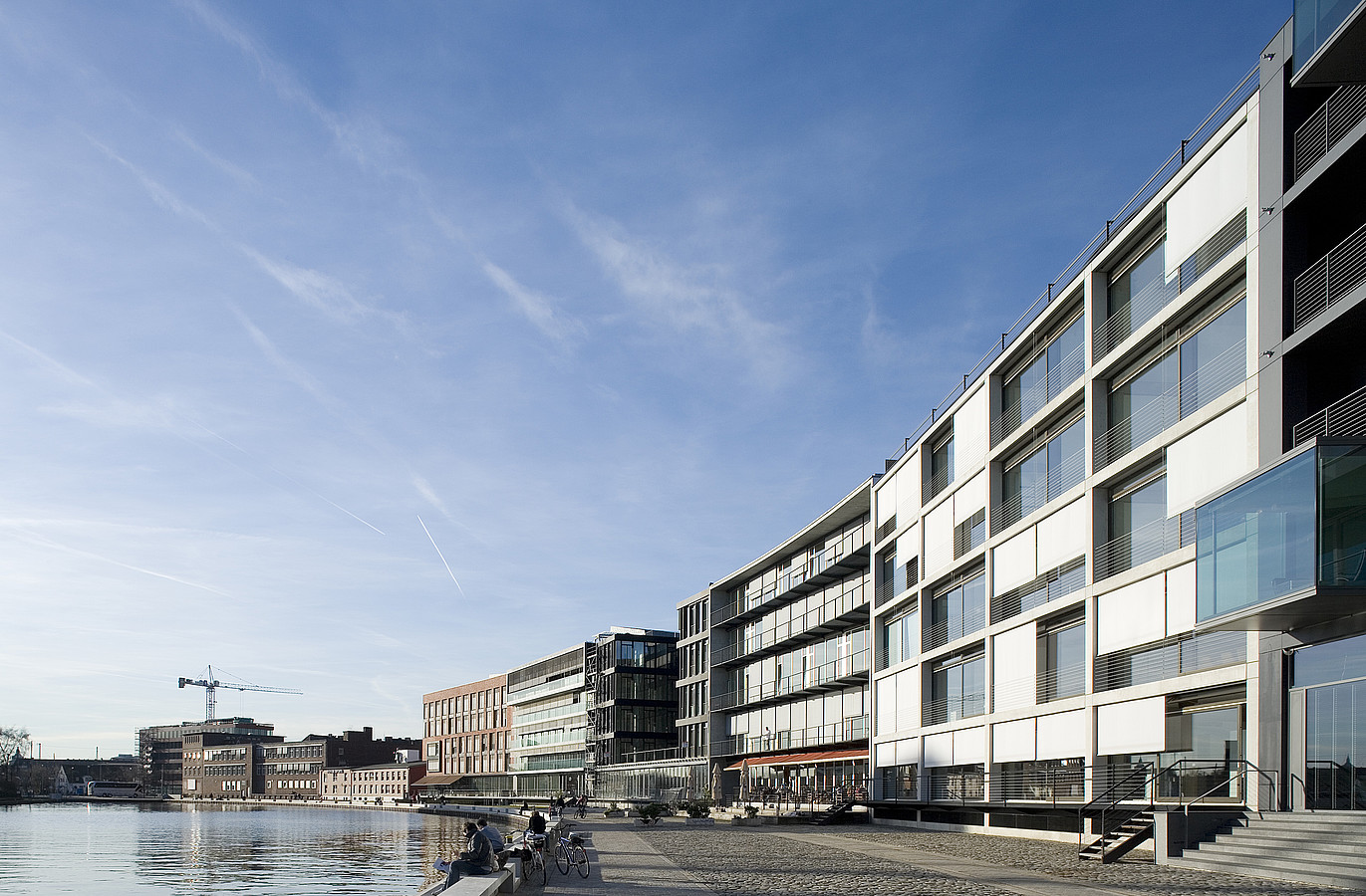 Bürohaus Hafenweg 24 Münster Das Bild zeigt eine Außenaufnahme des Neubaus, aus Richtung der Hafenpromenade, am Tag. Der Neubau befindet sich rechts im Bild, davor verläuft die Hafenpromenade. Links befindet sich das Hafenbecken.